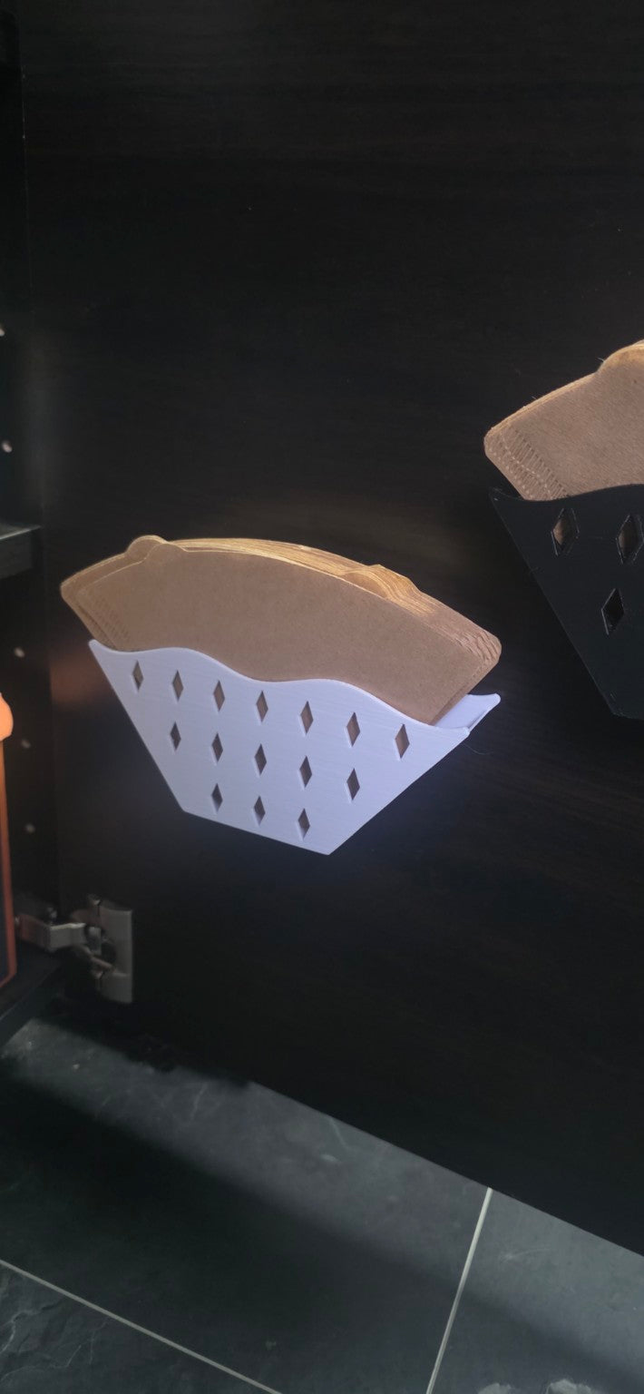 Weißer Kaffeefilterhalter mit Rautenmuster und Papierfiltern, innen an einer dunklen Schranktür befestigt.